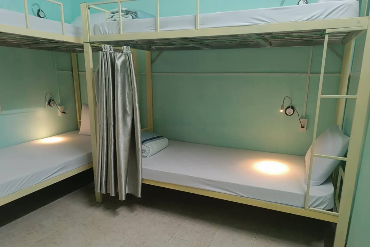 Une chambre avec un lit superposé, un rideau, des lampes de chevet et un sol carrelé.