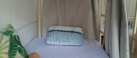 A single bed with a canopy, a rolled towel, and a pillow with a leaf pattern.