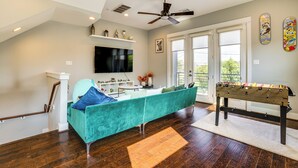 Un salon avec un canapé de couleur turquoise, une table de baby-foot et un téléviseur fixé au mur.