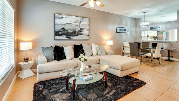 Ein modernes Wohnzimmer mit einem Ecksofa, einem Glastisch und einem Deckenventilator.