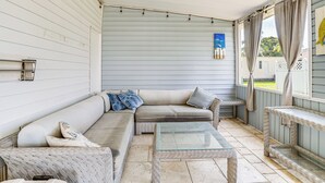 Un portico coperto con un divano in vimini, un tavolo con piano in vetro e una panca.