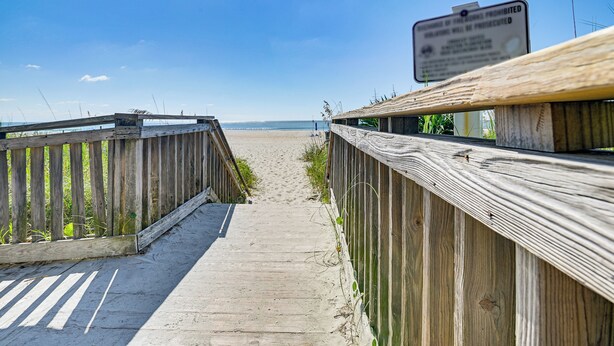 Un muelle de madera que conduce a una playa con un letrero de advertencia.