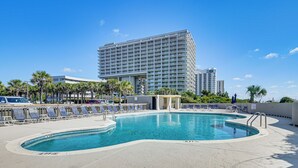 Un hotel con una piscina grande, palmeras y un edificio moderno al fondo.