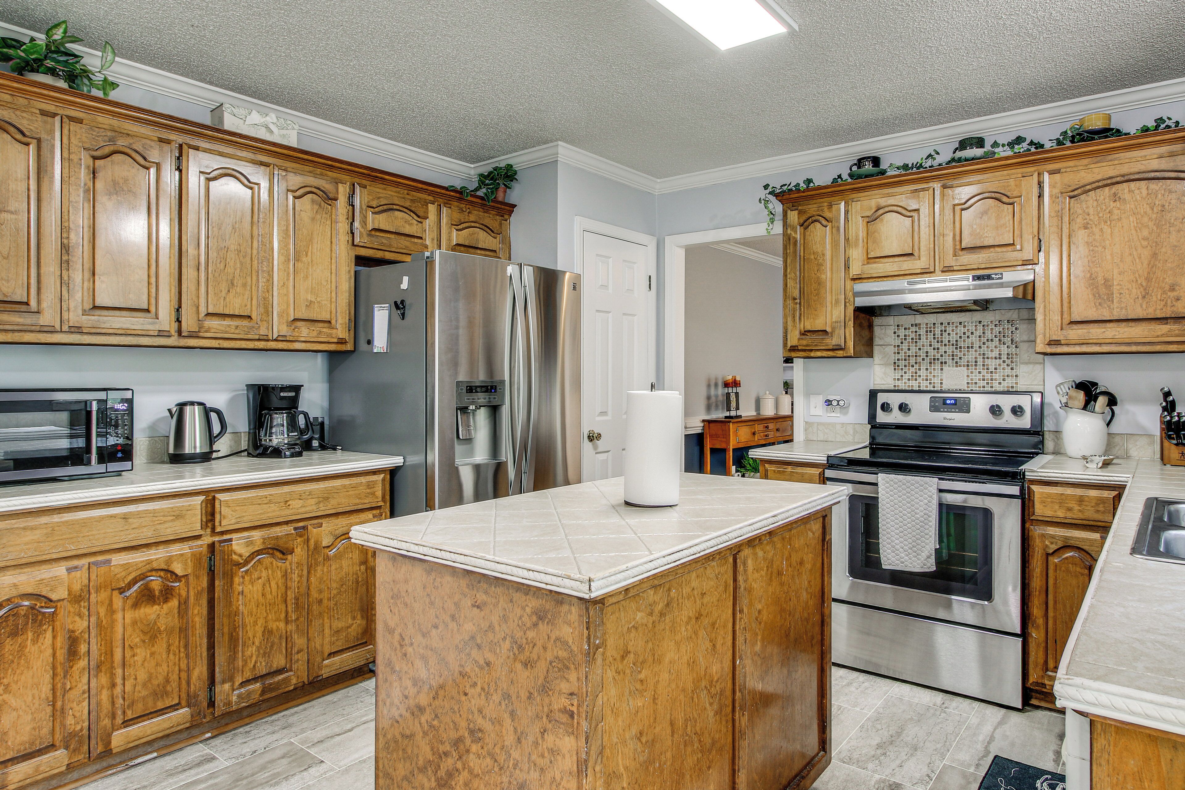 A kitchen with wooden cabinets, stainless steel appliances, a marble countertop, and a tiled backsplash.