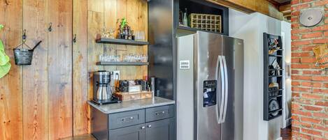 A compact kitchen with wooden walls, a stainless steel refrigerator, and a built-in wine rack.