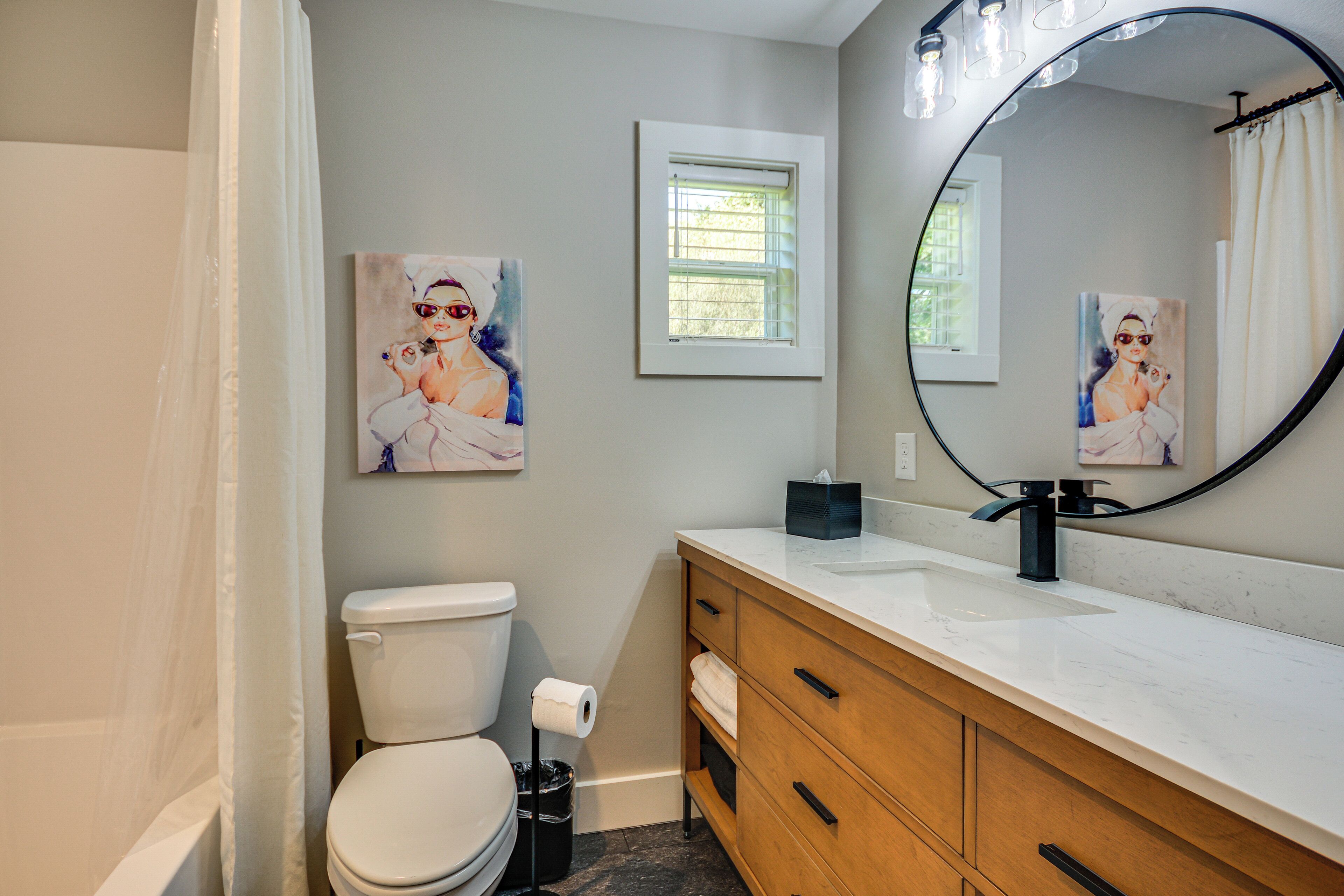 A bathroom with a toilet, a sink, a mirror, and two paintings on the wall.