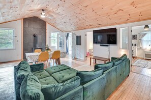 A spacious living area with a green sofa, wooden ceiling, and a television mounted on the wall. - Ice Fish, Snowshoe & Ski: Group Getaway in Summit (Summit)