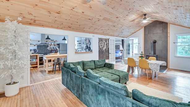 A spacious living area with a green sectional sofa, wooden flooring, a ceiling fan, and a dining area with yellow chairs. - Ice Fish, Snowshoe & Ski: Group Getaway in Summit (Summit)