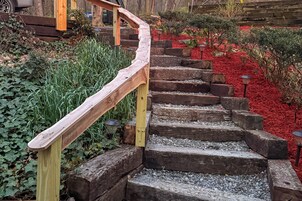 Una escalera de madera con barandilla curva, rodeada de follaje y acolchado rojo.