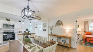 Une cuisine moderne avec des meubles blancs, une table à manger en bois et un luminaire suspendu.