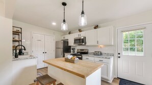 Une cuisine moderne avec des meubles blancs, un îlot central en bois et des luminaires suspendus.