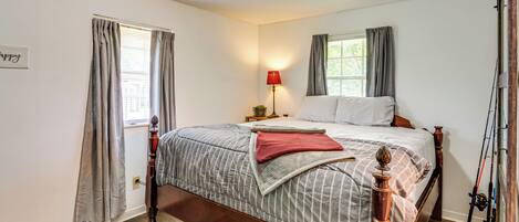A bedroom with a wooden bed, a nightstand, a lamp, and a window with curtains.