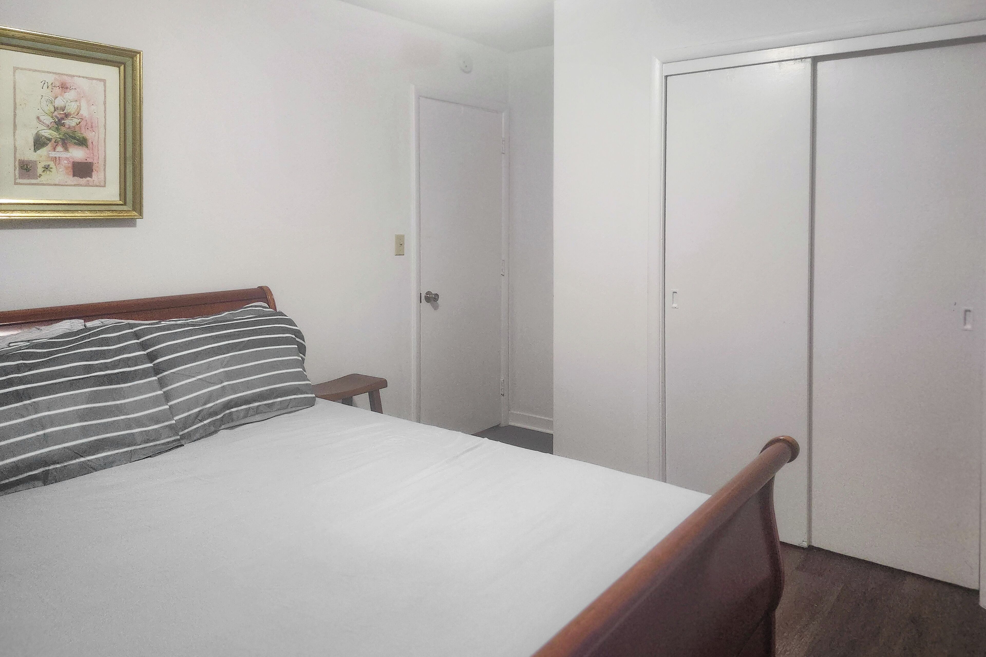Une chambre à coucher avec un lit, une table de chevet, un tableau encadré au mur et une armoire.