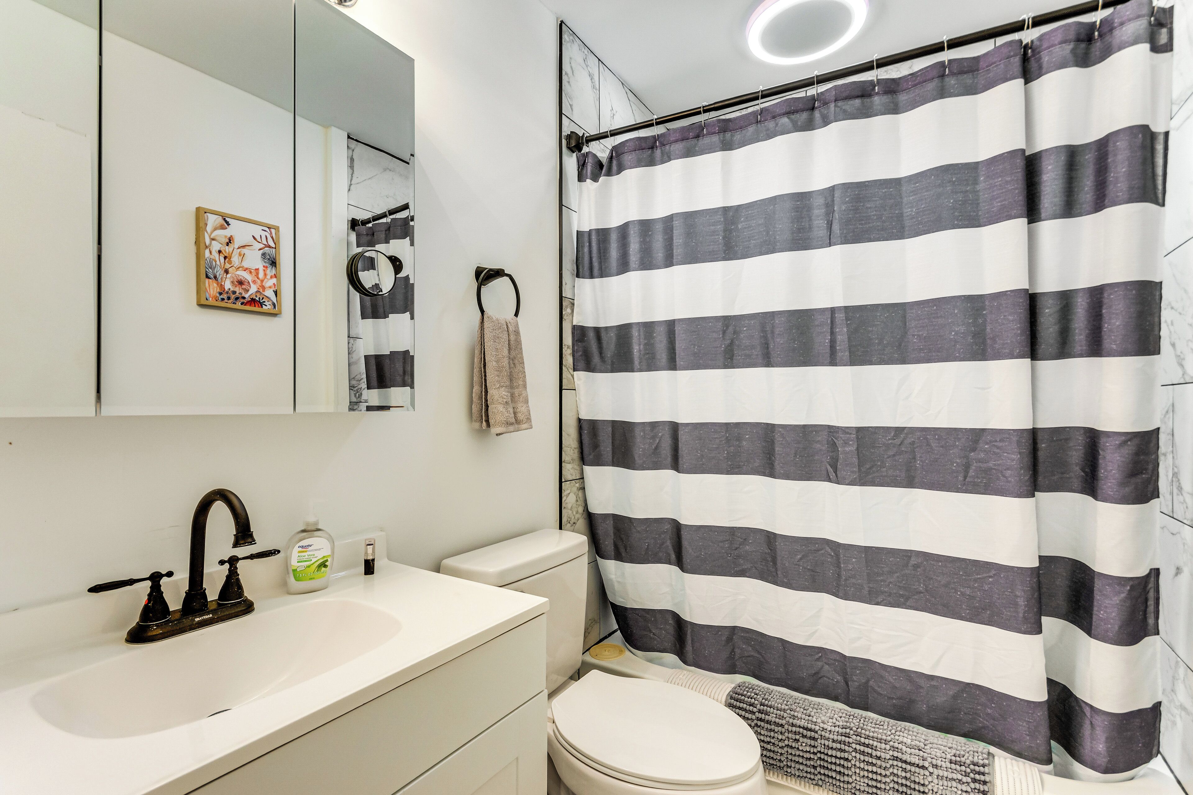 A bathroom with a white sink, black faucet, a toilet, a striped shower curtain, a towel ring, and a mirror.