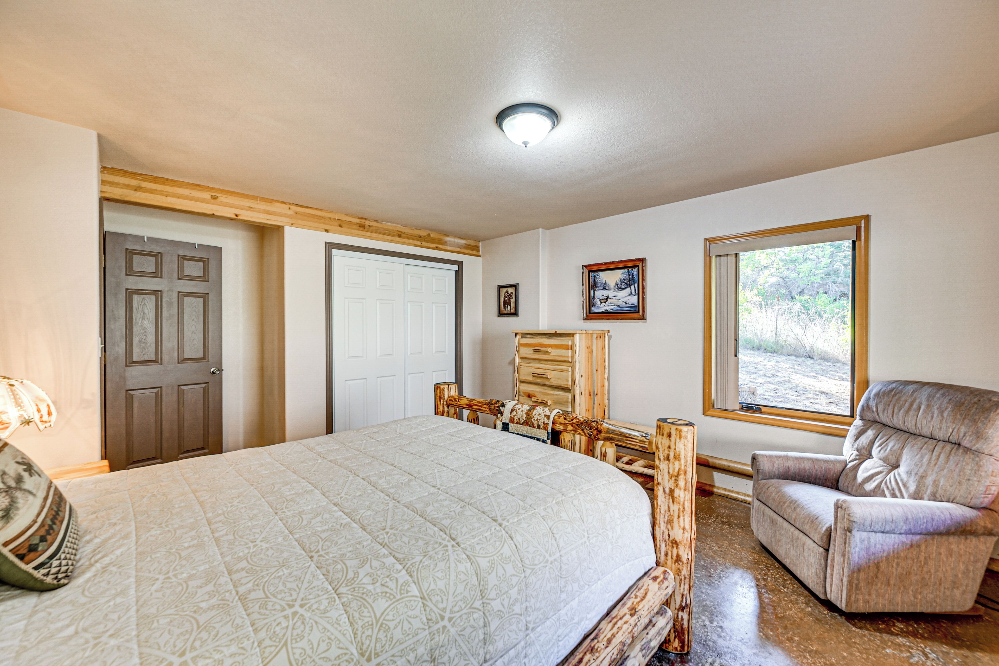 Un dormitorio con una cama grande, un aparador de madera, una silla y un ventanal con vistas al exterior.