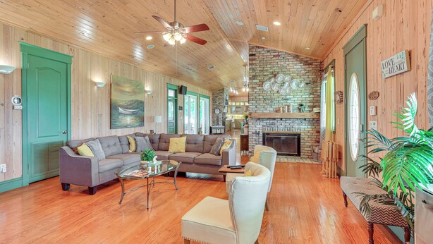A spacious living room with a fireplace, wooden floors, and a green door. - Private Hot Tub! Home < 1 Mi to Lake Okeechobee (Okeechobee)