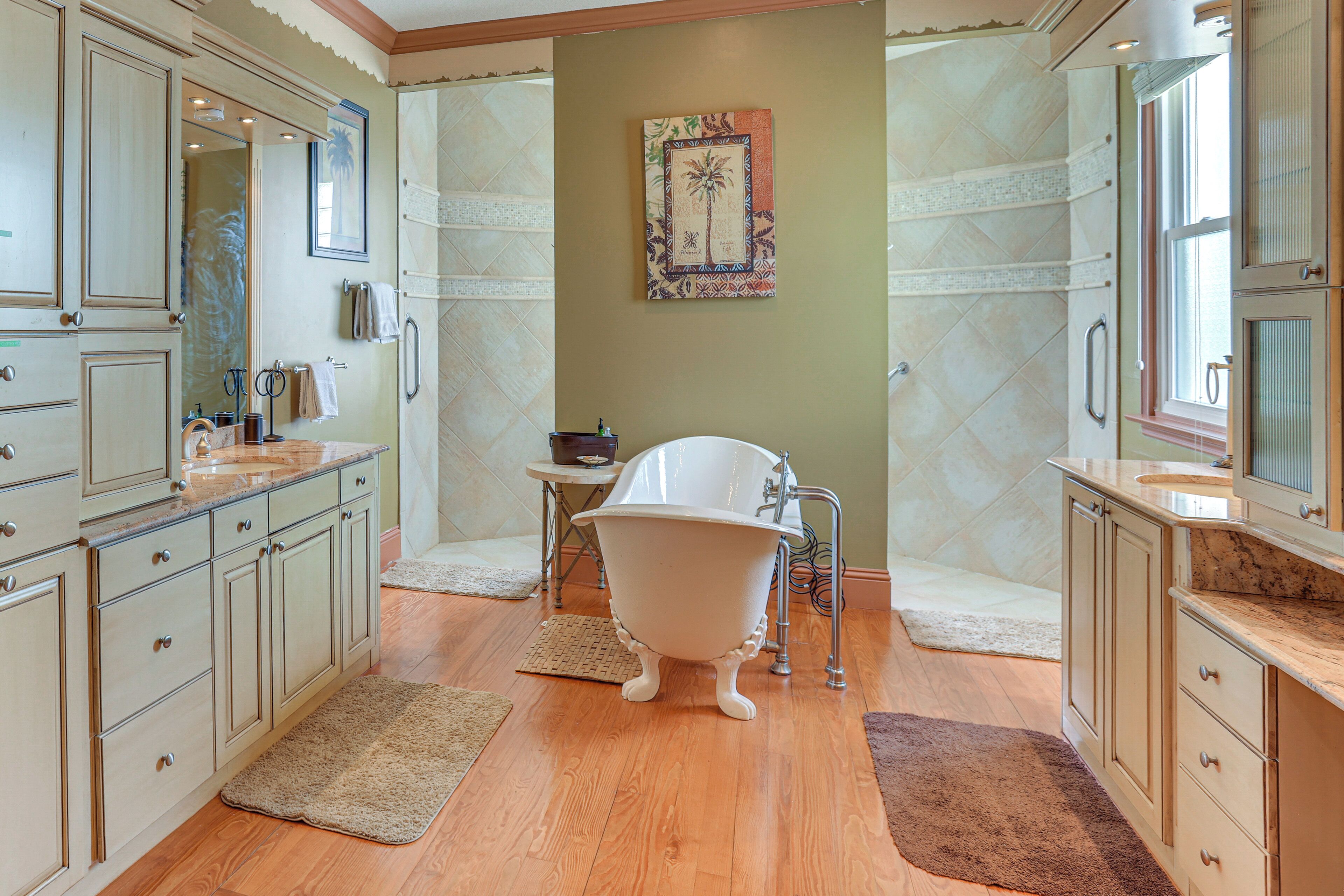 A bathroom with wooden floors, a clawfoot bathtub, and light-colored cabinetry.