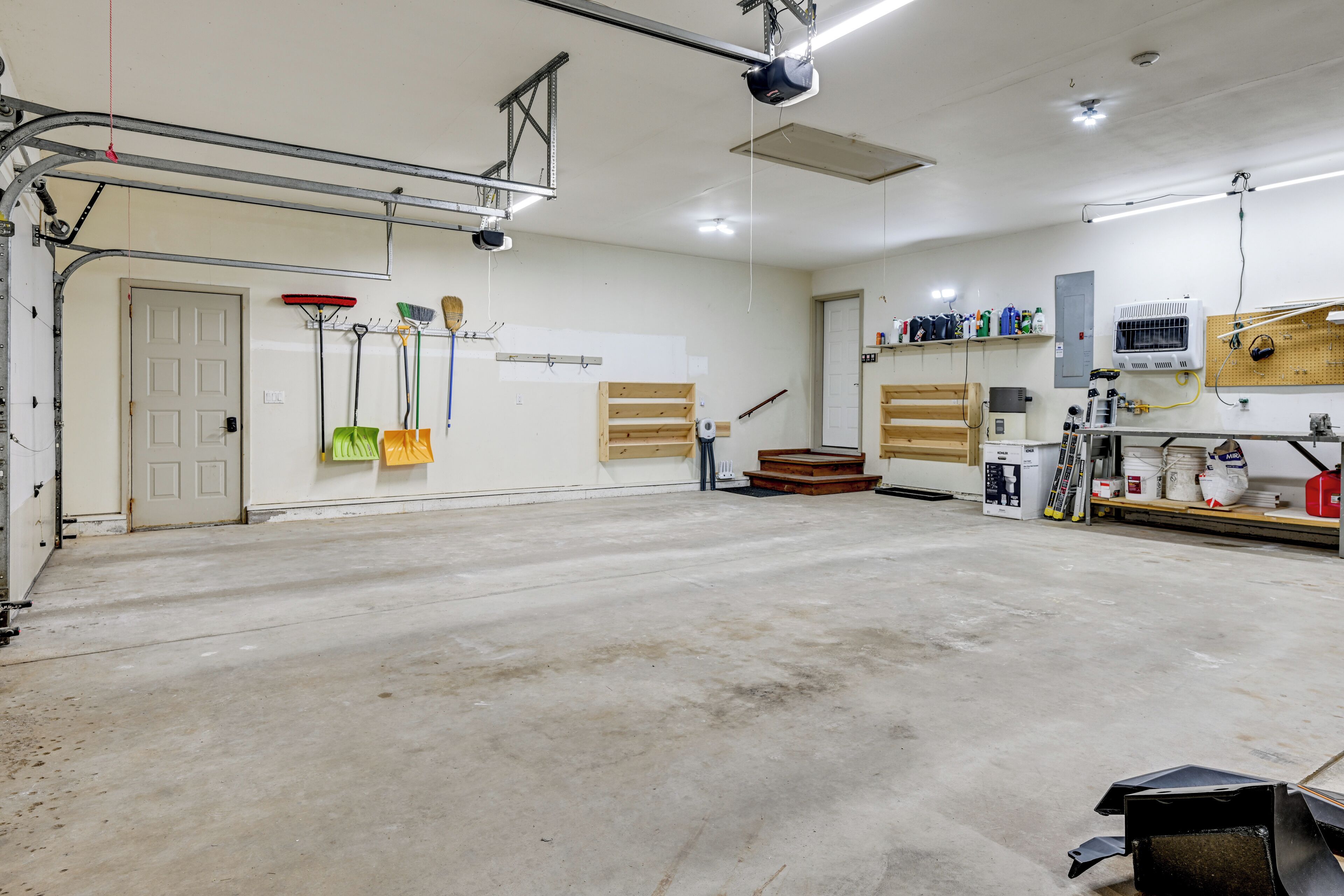 Un grand garage doté d’un sol en béton, d’une porte et de divers outils et équipements rangés sur des étagères.