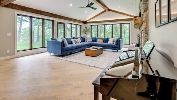 A spacious living room with a large sectional sofa, wooden flooring, and large windows offering a view of the outdoors.