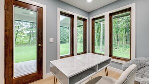 A room with a marble table, a chair, and large windows with a view of a green landscape.