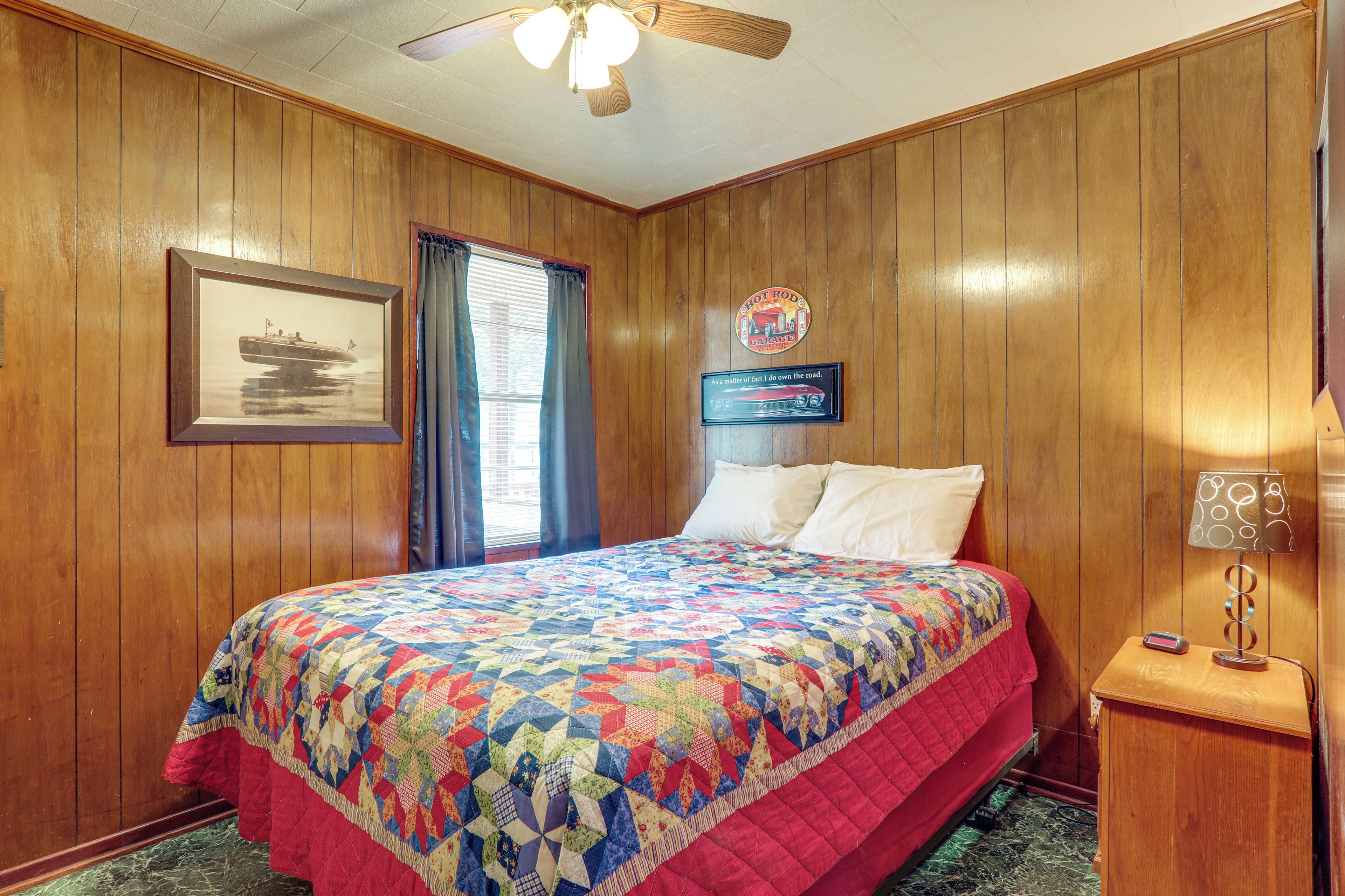 A wooden-paneled room with a bed, a framed picture, a sign, and a nightstand with a lamp.
