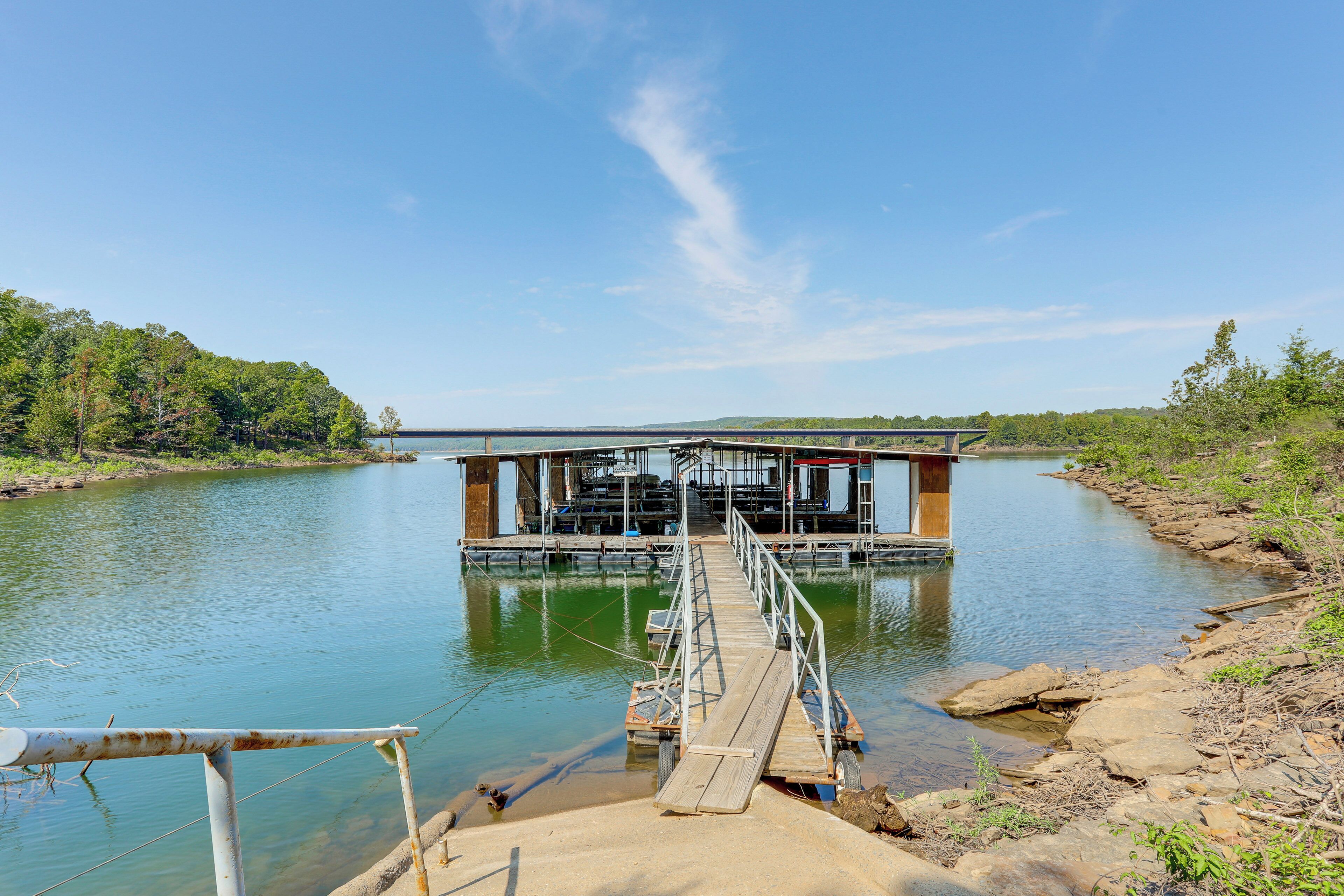 A wooden dock leading to a floating structure with a covered area, surrounded by calm water and greenery.