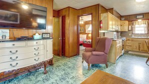 A spacious living room with a large flat-screen TV, a wooden cabinet, and a patterned armchair. - Walk to Greers Ferry Lake! Home w/ Dock Access (Higden)