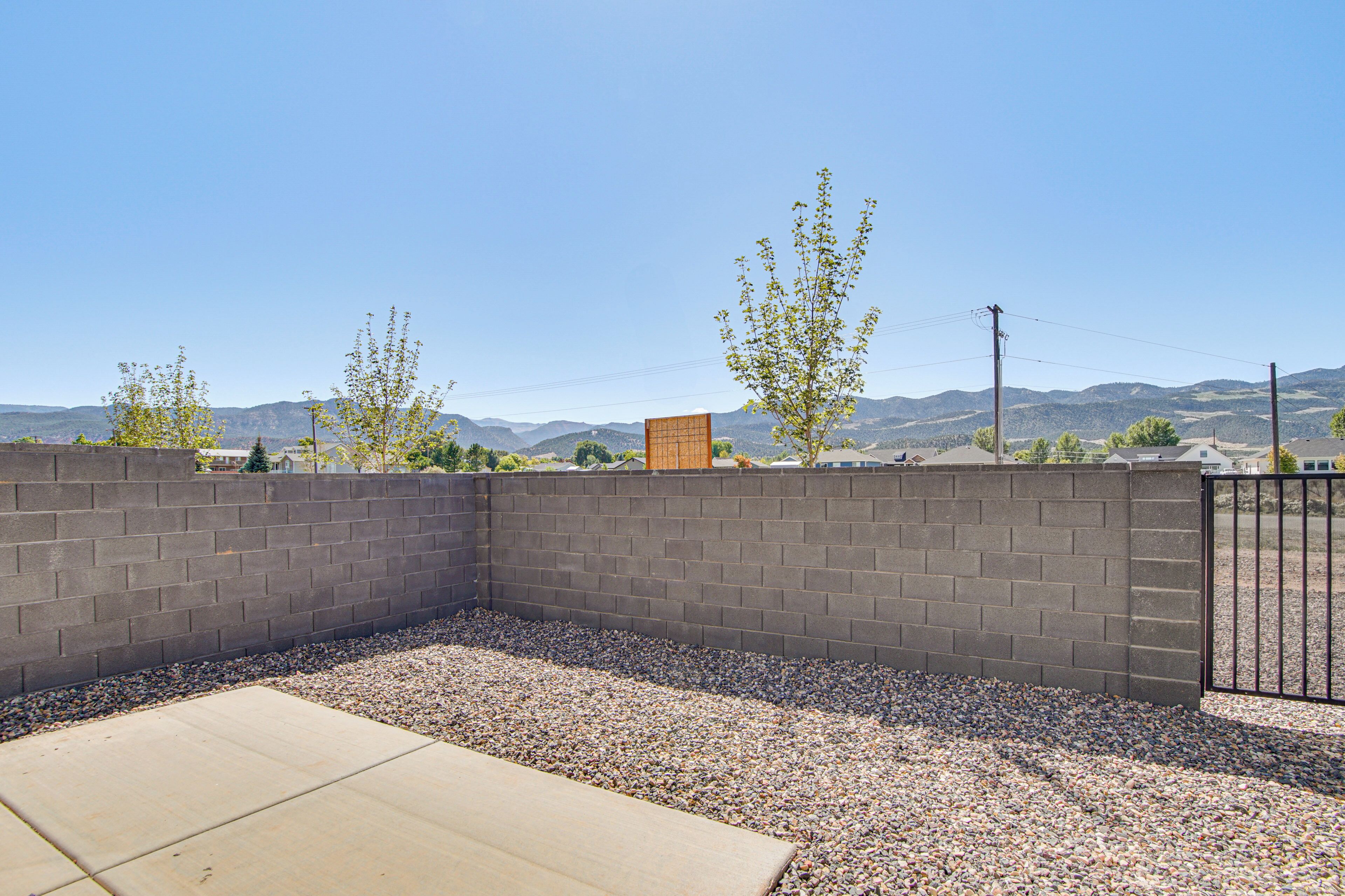 A backyard with a concrete patio, a brick wall, and a gravel area.