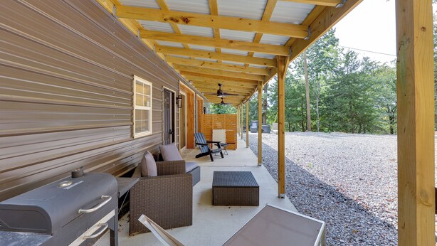 A covered patio with a grill, seating area, and a view of the surrounding trees. - Duplex w/ Furnished Patio Near Lake Ouachita! (Jessieville)