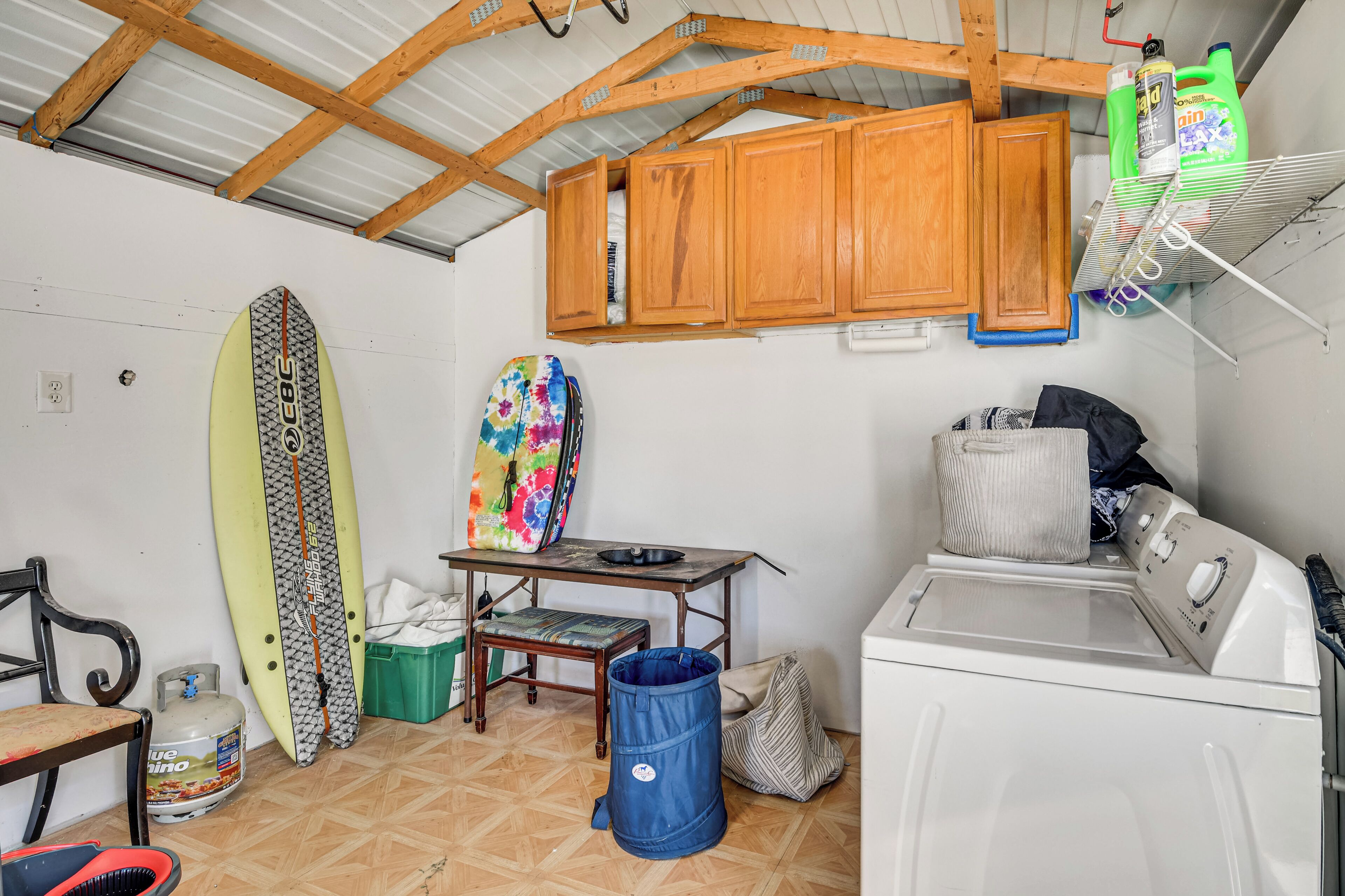 Een kleine keuken met houten kastjes, een wasmachine, een surfplank en een kleurrijke spijkerdoekhanddoek.