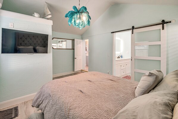 A bedroom with a large bed, a TV mounted on the wall, a mirror, and a sliding door closet.