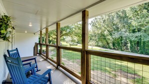 Un porche cubierto con barandas de madera y sillas azules, con vista a un patio cercado con árboles.