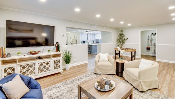 Una sala de estar moderna con un televisor de pantalla plana, sillones color beige, un sofá azul y una mesa de centro de madera.