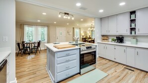 Una cocina moderna con suelo de madera, una isla central, armarios empotrados y una zona de comedor con mesa y sillas.