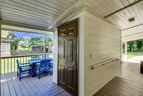 A covered porch with a wooden deck, a blue table and chairs, and a dark door. - Quiet Countryside Getaway in Appalachian Foothills (Commerce)