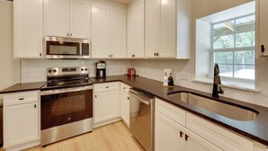 A modern kitchen with white cabinets, stainless steel appliances, a dishwasher, and a large window providing natural light.