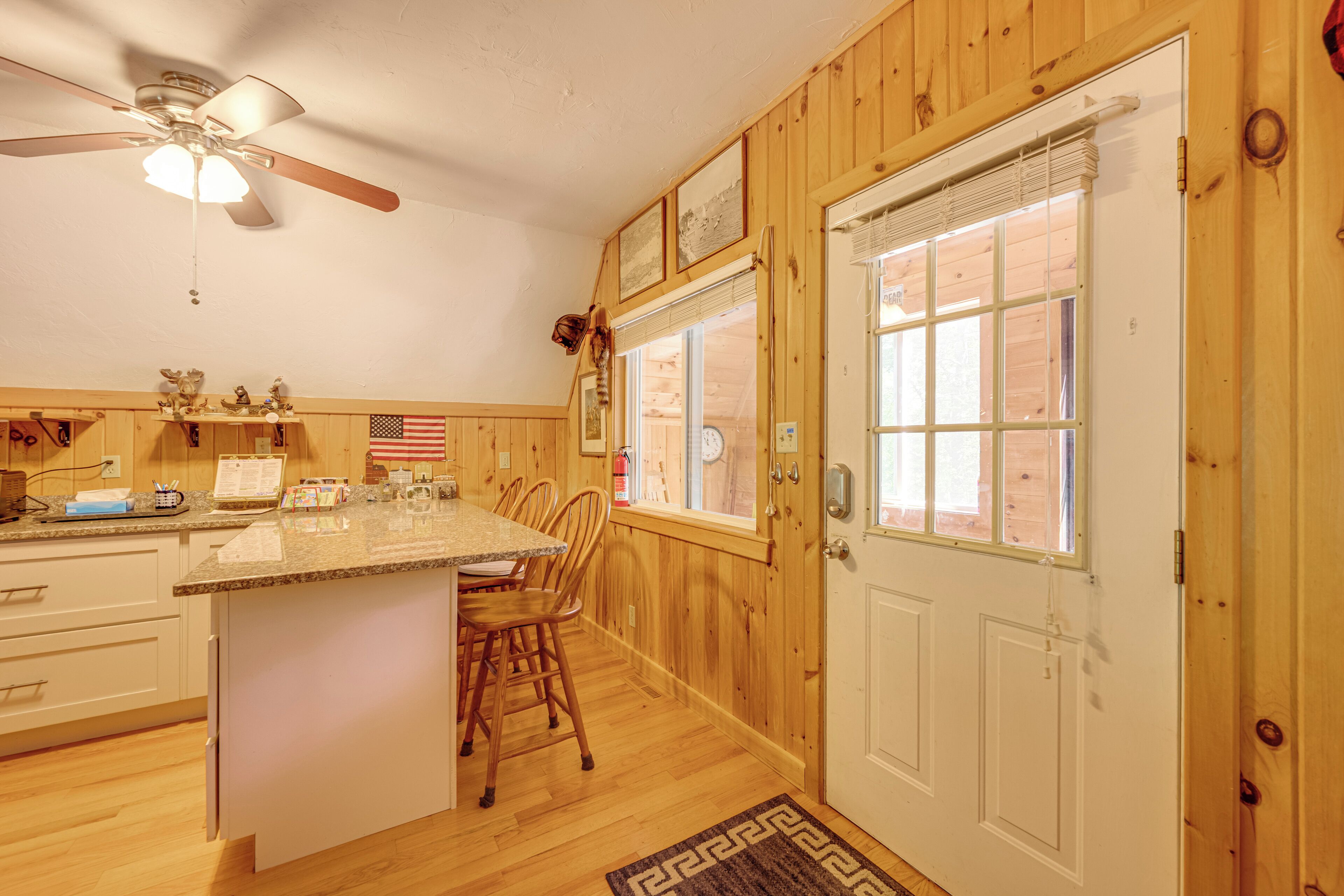 Interior de madera con isla de cocina, sillas, ventilador de techo y puerta con ventanas.