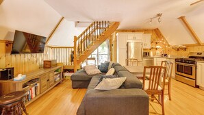 Ein geräumiges Loft mit einer Holztreppe, einem großen, grauen Ecksofa, einer Küche mit modernen Geräten und einem wandmontierten Flachbildfernseher.