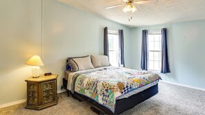 A bedroom with a bed, a nightstand with a lamp, a ceiling fan, and two windows with curtains. - 3 Mi to Dtwn: Pet-friendly Farm Retreat in Paris! (Paris)