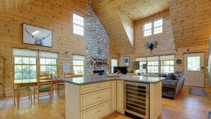 A spacious kitchen with a stone fireplace, wooden cabinets, and a large island. - Port Austin Cabin w/ Hot Tub: 1 Mi to Beach! (Port Austin)