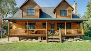 A two-story log cabin with a front porch, stone chimney, and a stone foundation. - Port Austin Cabin w/ Hot Tub: 1 Mi to Beach! (Port Austin)