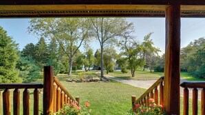 A wooden deck with a view of a well-maintained lawn and trees. - Port Austin Cabin w/ Hot Tub: 1 Mi to Beach! (Port Austin)