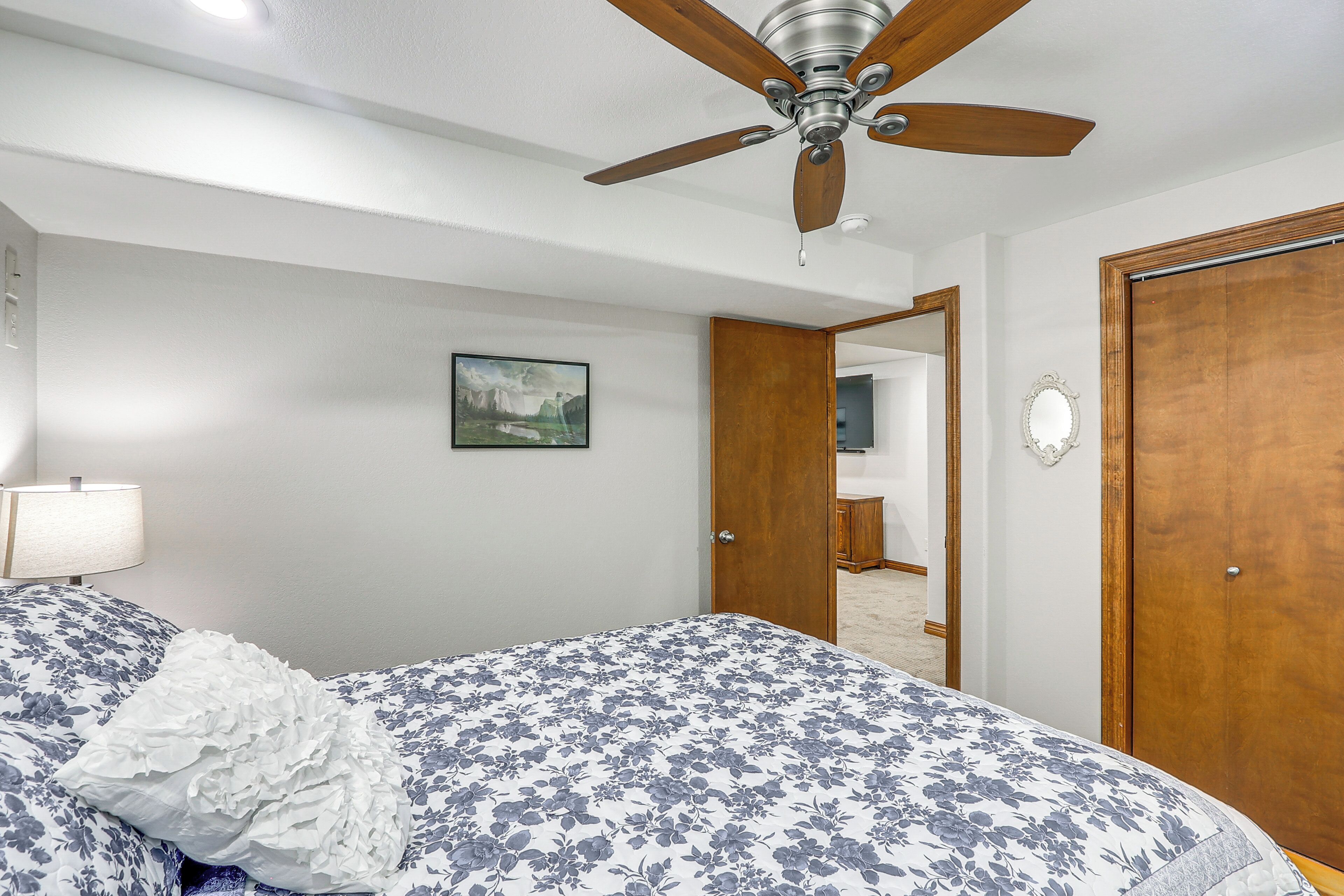 A bedroom with a bed, a ceiling fan, a wooden door, and a mirror.