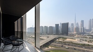 A balcony with two chairs and a table, overlooking a cityscape with high-rise buildings and a highway.