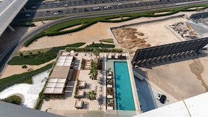 A high-rise hotel with a rooftop pool, a landscaped garden, and a view of a busy highway.