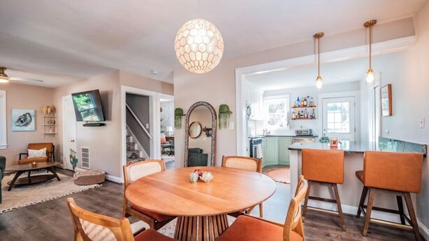 Un comedor amplio con una mesa y sillas de madera, una lámpara colgante grande y vistas a la cocina.