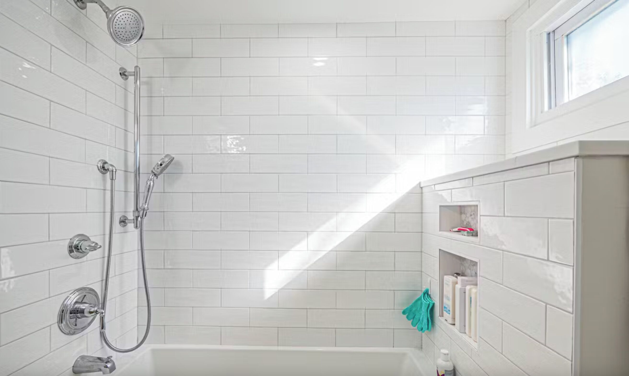 A modern bathroom with white tiles, a shower, a bathtub, and a shelf with toiletries.