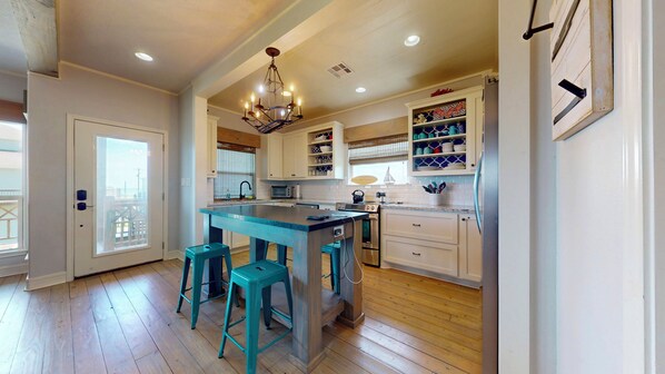 A modern kitchen with a central island, bar stools, white cabinetry, and a chandelier. - 977 Sailfish: 3 BR, 2 BA House in Crystal Beach, Sleeps 10 (Bolivar Peninsula)
