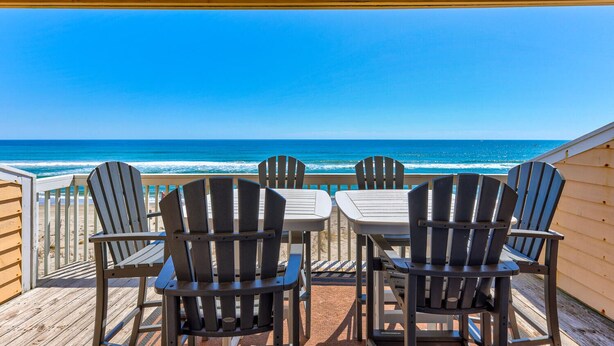 A wooden deck with four Adirondack chairs and a table, overlooking a beach with waves and clear blue sky. - Three Little Birds - Oceanfront Condo with Private Decks and Community Pools. Mu (Kure)