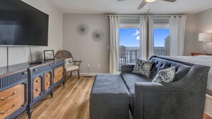 A modern living room with a flat-screen TV, wooden cabinet, grey sofa, and a ceiling fan. - Three Little Birds - Oceanfront Condo with Private Decks and Community Pools. Mu (Kure)